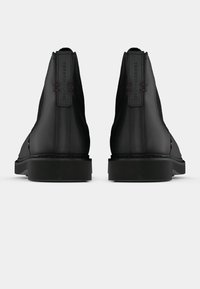 Botins de couro preto com textura suave, com painéis laterais elásticos, solas de borracha e detalhes sutis em costura vermelha.