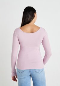 Langermet topp i lys rosa ribbet stoff, med vid ryggen erme og tettsittende design, kombinert med lyseblå jeans.