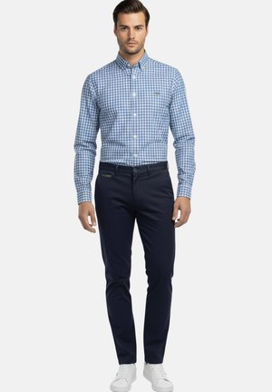 Camisa de botones a cuadros azul y blanca, pantalones azul marino y zapatillas blancas. Con mangas largas y corte ajustado. Diseño simple sin estampados.