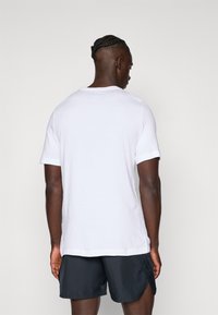 Tricou alb cu mânecă scurtă din bumbac, cu decolteu rotund și o croială relaxată, asociat cu pantaloni scurți negri.