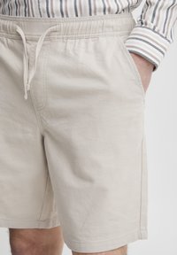 Beige bomullsshorts med elastisk midje og snøring. Har to sidelommer og en glatt tekstur.