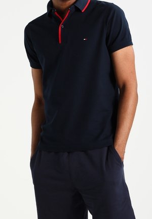 Polo bleu marine avec accents rouges, manches courtes, col à boutons et détail logo sur la poitrine. Matière en coton lisse avec une coupe ajustée.