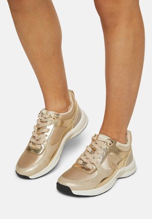 Las zapatillas metálicas doradas tienen una textura suave, forma redondeada y cordones suaves. Los acentos incluyen paneles laterales y una suela acolchada.
