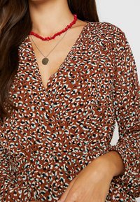 Robe portefeuille marron présentant un motif léopard en noir, blanc et bleu clair. Le col est en forme de V, avec des manches longues.