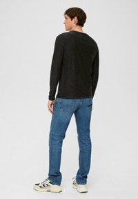 Zwarte longsleeve shirt met een ronde hals, gecombineerd met blauwe jeans. De outfit wordt compleet gemaakt met grijze en zwarte sneakers.