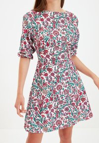 Kleid mit Blumenmuster auf weißem Grund, mit einer Vielzahl von pinken, roten und grünen Blumen. Kurze Puffärmel und eine taillierte Passform.