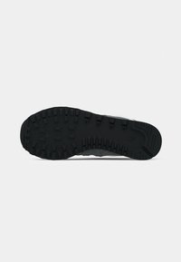 Sort gummisål på en sneaker med mønstrede riller til greb, sat mod en ensfarvet hvid baggrund.