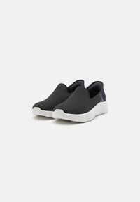 Czarne siatkowe buty wsuwane charakteryzują się lekką konstrukcją, białą gumową podeszwą oraz gładką fakturą z minimalnym brandingiem po boku.