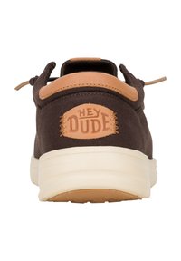 Scarpa in tela marrone con un accento in pelle beige, caratterizzata da un logo circolare "HEY DUDE" sul tallone, punta arrotondata e suola imbottita.
