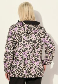 Leopardmönstrad jacka med en blandning av svarta, krämfärgade och lila färger, med huva och elastiska ärmslut, tillverkad av ett lätt material.