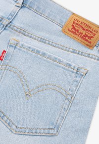 Šviesiai mėlyni džinsai iš džinsinio audinio, klasikinio dizaino, su auksinio siūlės siuvimu ir raudona logotipo etikete. Užpakalinėje kišenėje yra širdies formos siuvinėto detalių.