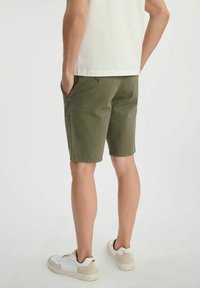 Oliwkowe szorty o dopasowanym kroju, z bocznymi kieszeniami, prostą talią i w połączeniu z białymi trampkami. Gładki, lekki materiał.