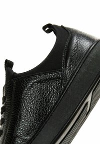 Scarpa nera con tomaia in pelle texturizzata, pannelli elastici e suola in gomma con base decorata per aderenza e flessibilità.