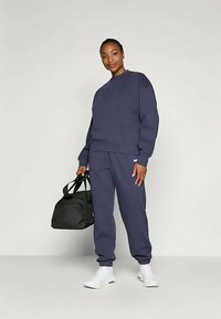 Tengerészkék melegítő szett puha anyagból, rövidujjú pulóverrel és rugalmas derekú nadrággal, fekete sporttáskával párosítva.