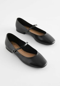 Ballet flats in pelle nera con punta quadrata, tacco basso e una sottile fascia sul piede con dettaglio a fibbia. Interno beige.