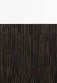Close-up van donkerbruine ribfluweelstof met verticale ribbels en stiksels langs het taille gedeelte.