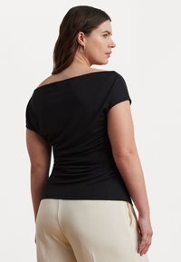 Haut noir à manches courtes avec un large décolleté hors-épaule, au design ajusté et à la texture froncée à l'arrière. Assorti à un pantalon de couleur claire.