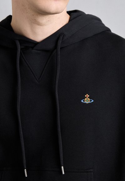 Schwarzer Hoodie mit einer Vordertasche, ausgestattet mit Kordeln und einem kleinen farbigen Emblem eines Schiffs innerhalb eines blauen Kreises. Glatte Textur.