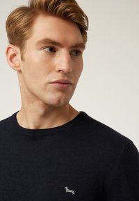Maglione a maglia blu navy con collo rotondo e un piccolo logo di un cane ricamato sul lato sinistro del petto. Texture morbida con un design aderente.