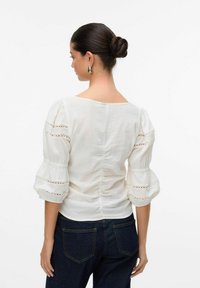 Blusa di cotone bianca con maniche a sbuffo, con dettagli in pizzo sulle maniche e una schiena aderente, abbinata a jeans in denim scuro.