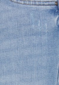 Tecido de denim azul claro com uma textura subtil, apresentando detalhes desgastados e costura. Inclui um botão de metal e fecho de zíper.