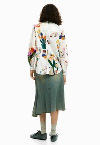 Õie mustriga pluus erksates värvides, kerge kangas; sobitatud rohelise teksaseelikuga, millel on kihiline ääredetail.