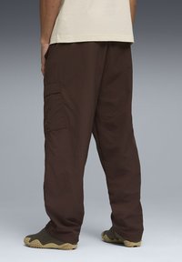Pantalon cargo marron en tissu léger, présentant une coupe décontractée, des poches latérales et une forme droite, assorti de chaussures sombres texturées.