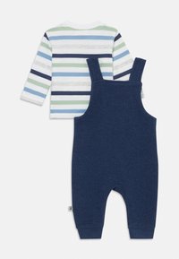 Camicia di cotone a maniche lunghe con righe blu, verdi e bianche abbinata a salopette blu a costine con spalline regolabili e una texture morbida.