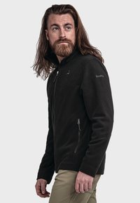 Zwarte fleece jas met volledige ritssluiting, zijzakken en een zachte textuur. Heeft een subtiel logo op de borst en de arm.