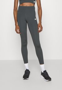 Leggings a vita alta di colore grigio scuro, realizzati in tessuto elastico con cuciture piatte; presentano un piccolo logo bianco sulla coscia superiore.