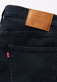 Mörkblå Levi's jeans bakficka med brun läderetikett från Levi Strauss & Co. som visar storlek W32 L32 och röd Levi's-tag på fickans söm.