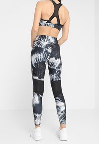 Czarny i biały zestaw sportowy, w skład którego wchodzi biustonosz sportowy z plecami w racerback oraz legginsy z wysokim stanem, ozdobione graficznym wzorem i akcentami z siateczki.