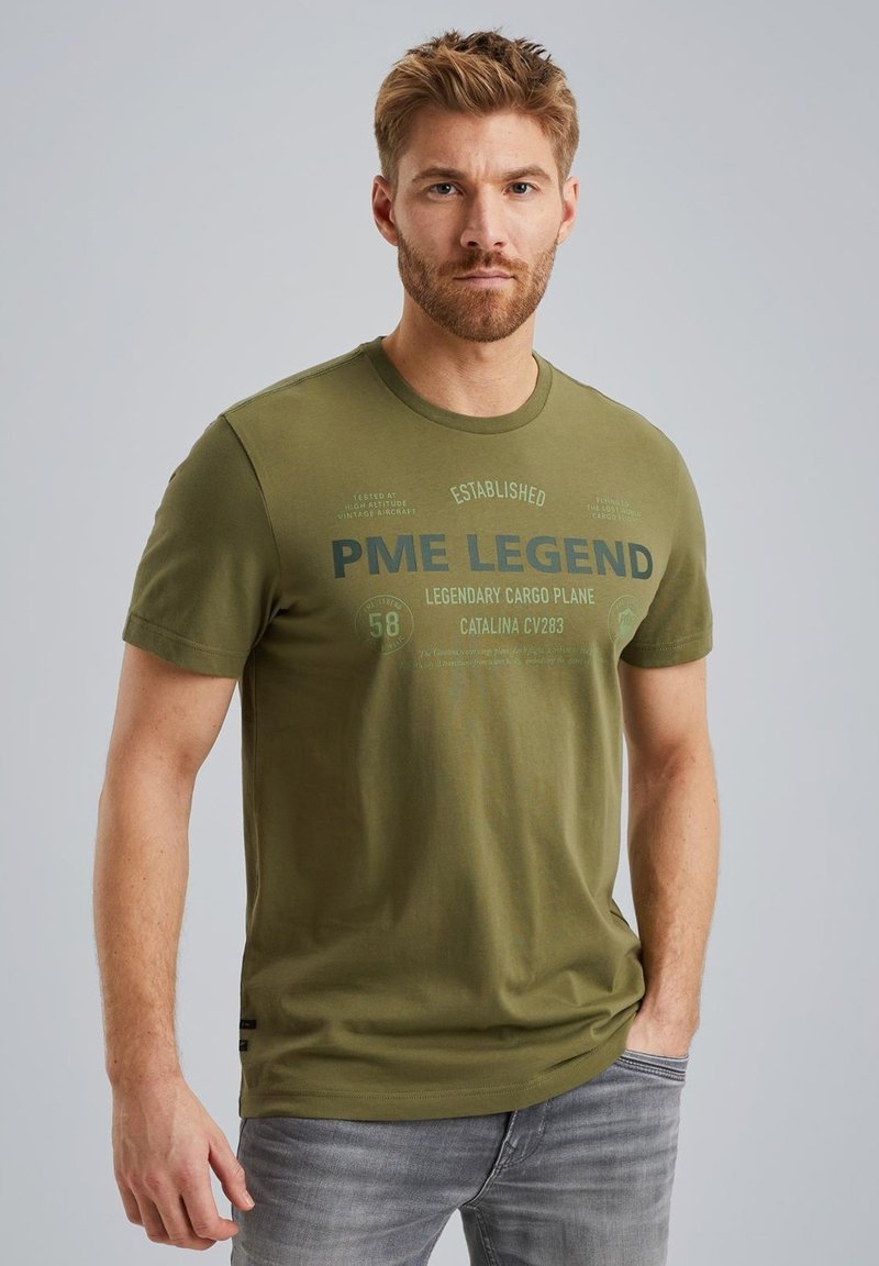 Olive zelené bavlnené tričko s krátkymi rukávmi a okrúhlym výstrihom. Obsahuje potlačený text vrátane "PME Legend" a letecké detaily.