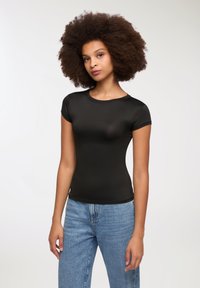 T-shirt aderente nero realizzato in un tessuto liscio e elastico. Maniche corte, scollatura a girocollo e silhouette aderente. Abbinato a jeans blu.