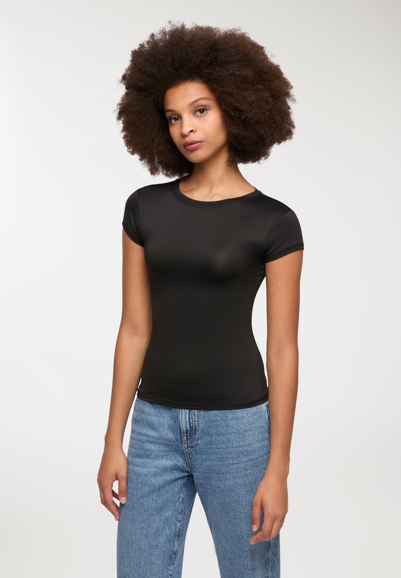 T-shirt aderente nero realizzato in un tessuto liscio e elastico. Maniche corte, scollatura a girocollo e silhouette aderente. Abbinato a jeans blu.