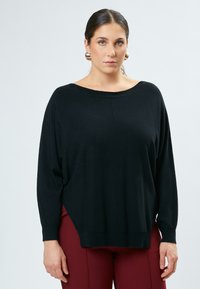 Maglione nero oversize con scollatura ampia, polsini e orlo a costine. Tessuto morbido, maniche lunghe, abbinato a pantaloni aderenti bordeaux.