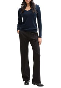 Pull en V navy en tissu doux associé à un pantalon noir ajusté. Les chaussures sont en cuir noir brillant. La tenue présente une coupe décontractée et un design minimaliste.