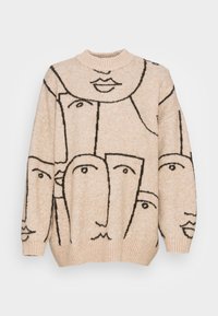 Beige oversized tröja med abstrakta svarta ansiktsmönster. Hög krage, ribbade ärmslut och nederkant. Mjuk stickad textur.