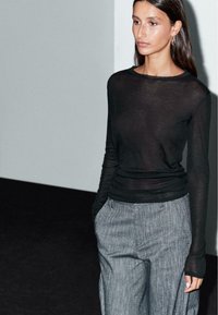 Black long-sleeve top with a sheer texture paired with grey pinstripe trousers, featuring side pockets and a tailored fit.