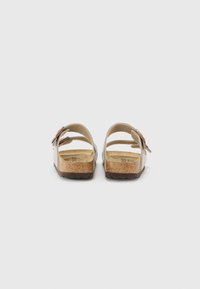 Sandalias marrones y beige con correas ajustables, plantilla suave y suela de goma texturizada. Presentan un diseño minimalista y perfil plano.