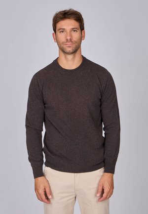 Pull noir, à manches longues, en matériau doux, avec col rond et poignets côtelés, porté sur un pantalon beige.