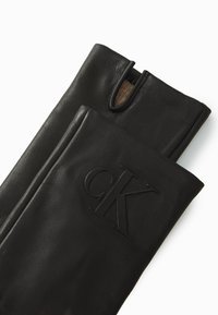 Sorte skinnhansker med en glatt tekstur, med et utskåret område ved knokene og en preget "CK"-logo på mansjetten.