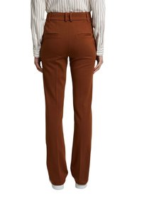 Hnědé kalhoty se střihem rovného nohavice, dvěma zadními kapsami a pasem s poutky na opasek. Kombinováno s pruhovanou košilí a bílými teniskami.