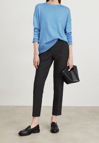 Pull en maille bleu avec des épaulettes tombantes, pantalon noir ajusté, mocassins noirs et un petit sac noir avec une anse découpée.