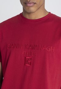 Röd bomulls-t-shirt med broderad märkning "GIANNI KAVANAGH ATELIER" och en logotyp på framsidan; rund halsringning och korta ärmar.