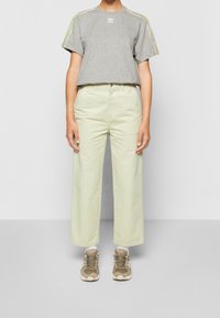 Grå bomullströja med korta ärmar och gröna accentlinjer. Ljusgröna vida byxor och beige sportskor.