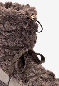 Bota marrón difusa con una textura suave, base de gamuza gris, cordones de punto y acentos de hardware dorado cerca de la parte superior.