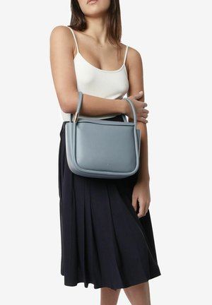 Sac à main en cuir bleu clair avec une forme structurée, des poignées courtes et une texture lisse, porté au-dessus d'une jupe plissée noire.