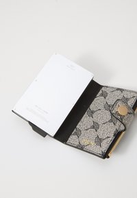 RFID-blocking wallet with silver card holder, black fabric interior, and a patterned exterior in beige and black. Gold zipper and snap fastener.