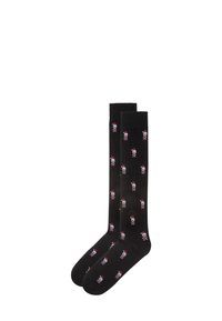 Black knee-high socks with repeated white skull and red Santa hat design. Smooth texture, elastic top, suitable for casual wear.